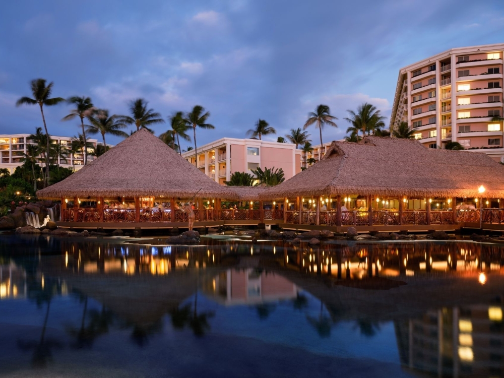 The exterior of Humuhumunukunukuapuaa restaurant - an oceanfront thatched roof building illuminated by lanterns