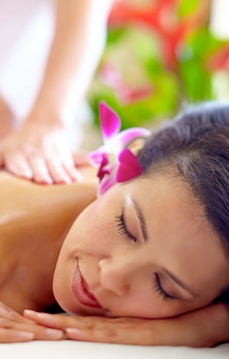 a woman with a pink flower behind her ear lays on her stomach while a therapist massages her back