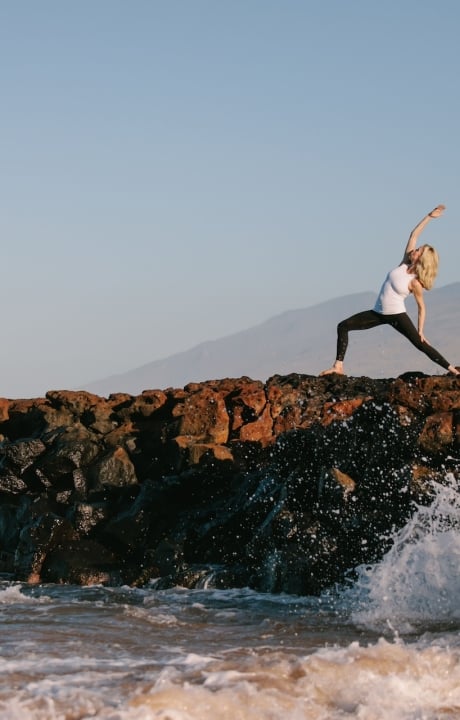 A woman doing yoga on a rock adjacent to the ocean