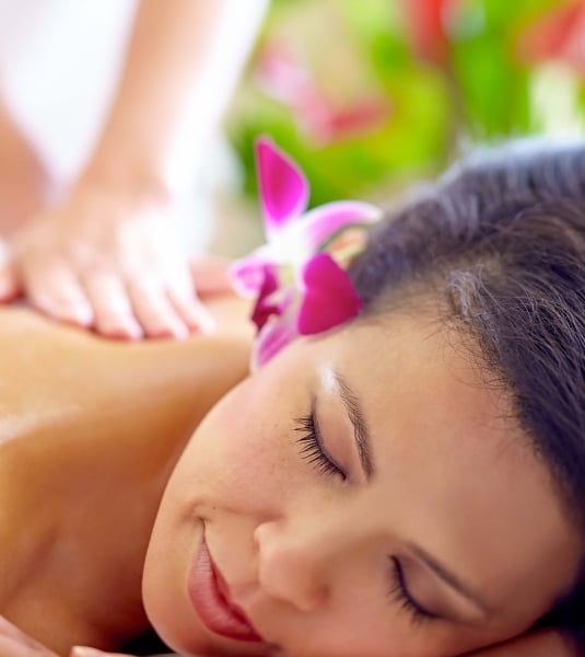 a woman with a pink flower behind her ear lays on her stomach while a therapist massages her back