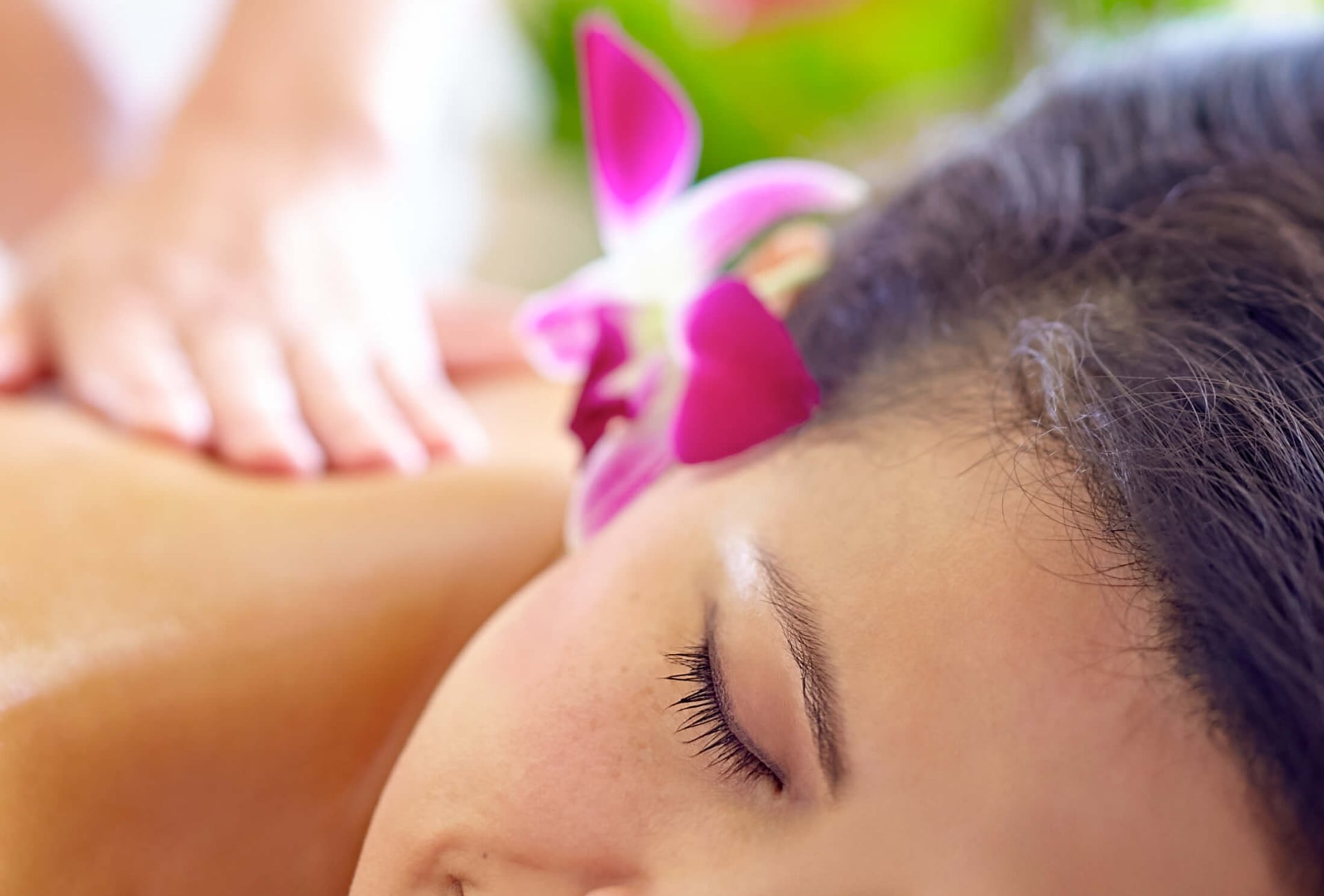 a woman with a pink flower behind her ear lays on her stomach while a therapist massages her back