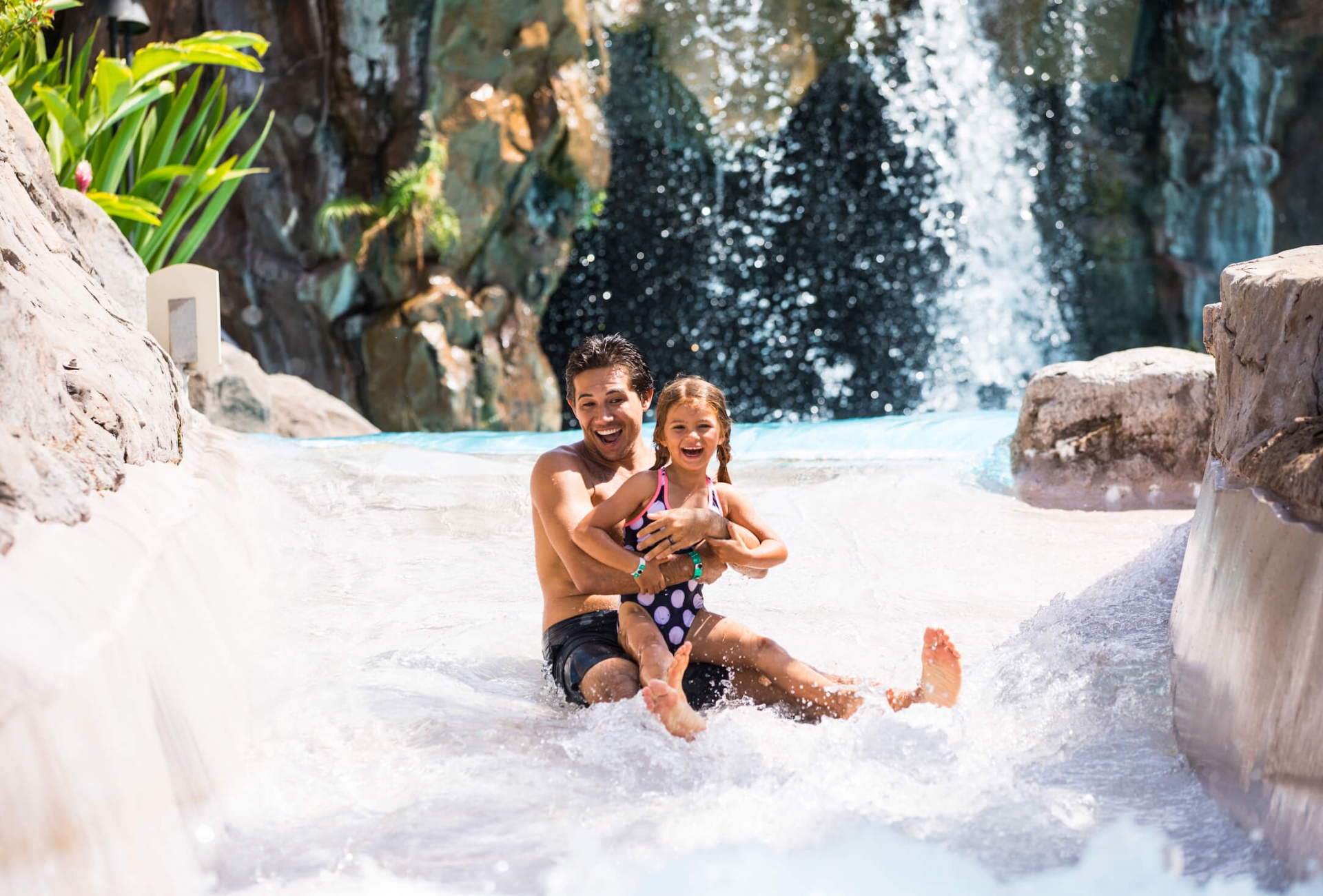 man and child in bathing suits slide down a water slide