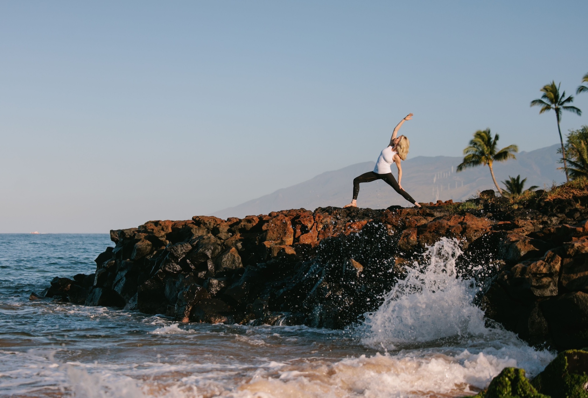 A woman doing yoga on a rock adjacent to the ocean