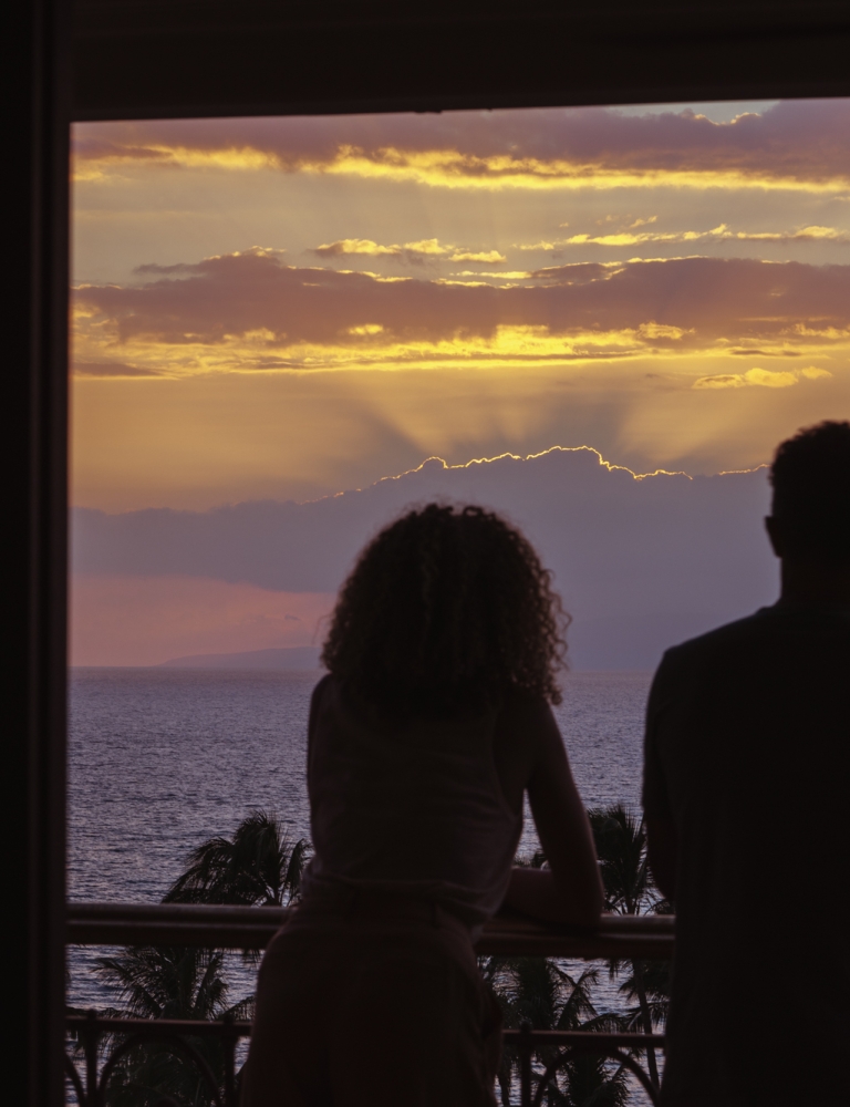 A couple looks out on the ocean from their balcony at dusk